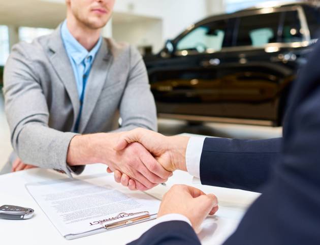 Close up of handsome client shaking hands with sales manager after signing purchase contract to buy new car in showroom